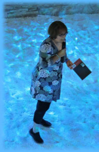 Susan performs her poetry in what appears to be a vivid blue shimmering underwater venue.